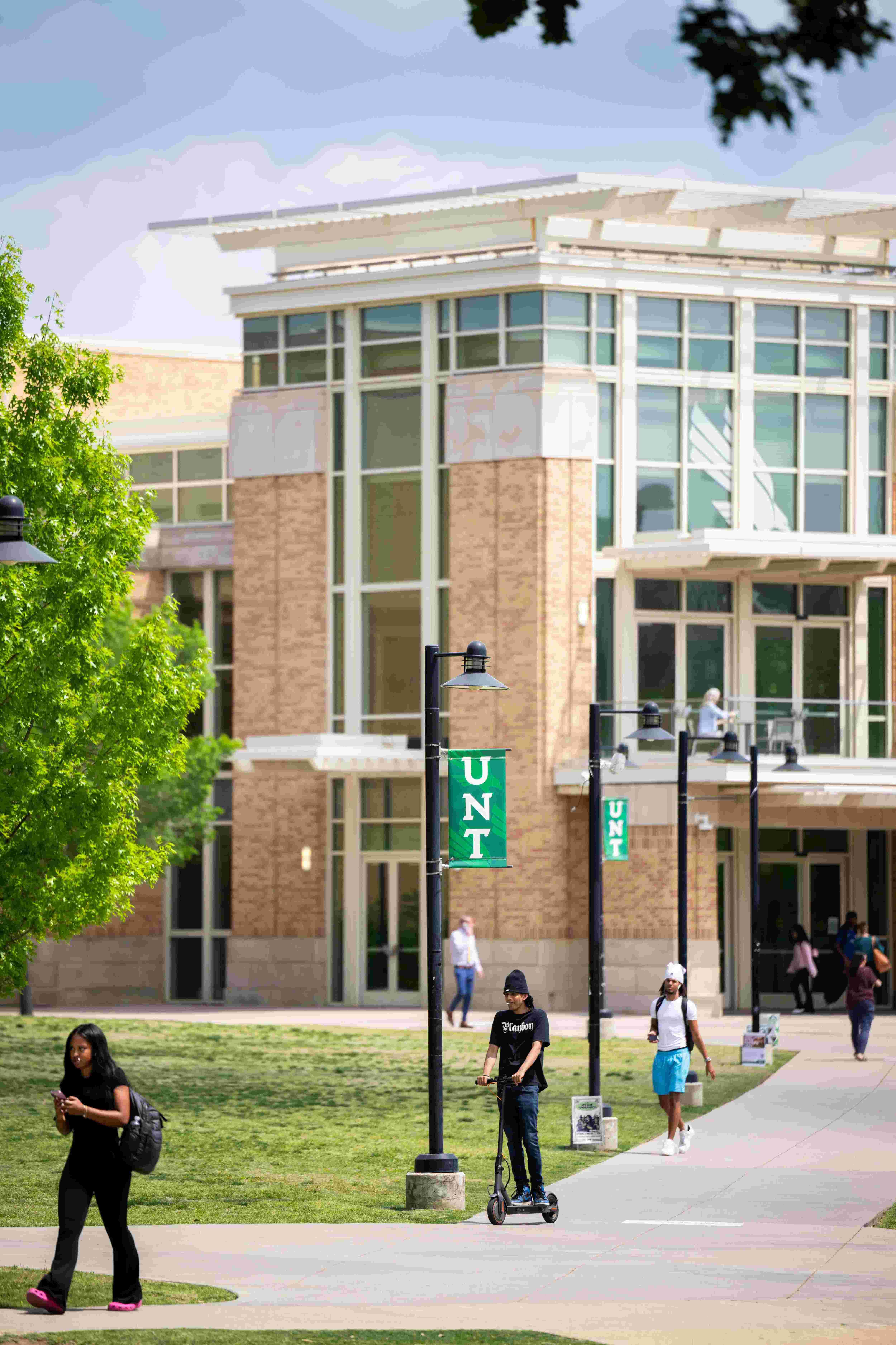 Students walking across campus with one student on a scooter